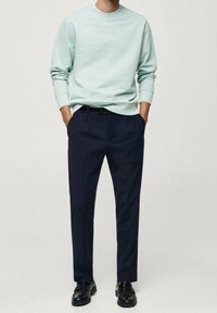 Helles blaues Sweatshirt aus weichem Material, kombiniert mit navyblauen, maßgeschneiderten Hose mit einem entspannten Schnitt und geraden Beinen. Schwarze Schuhe runden das Outfit ab.
