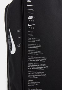Svart Nike-tyg med flera vita Nike Air-logotyper och flerspråkig text om Air-Sole innersulor och varumärkesinformation.