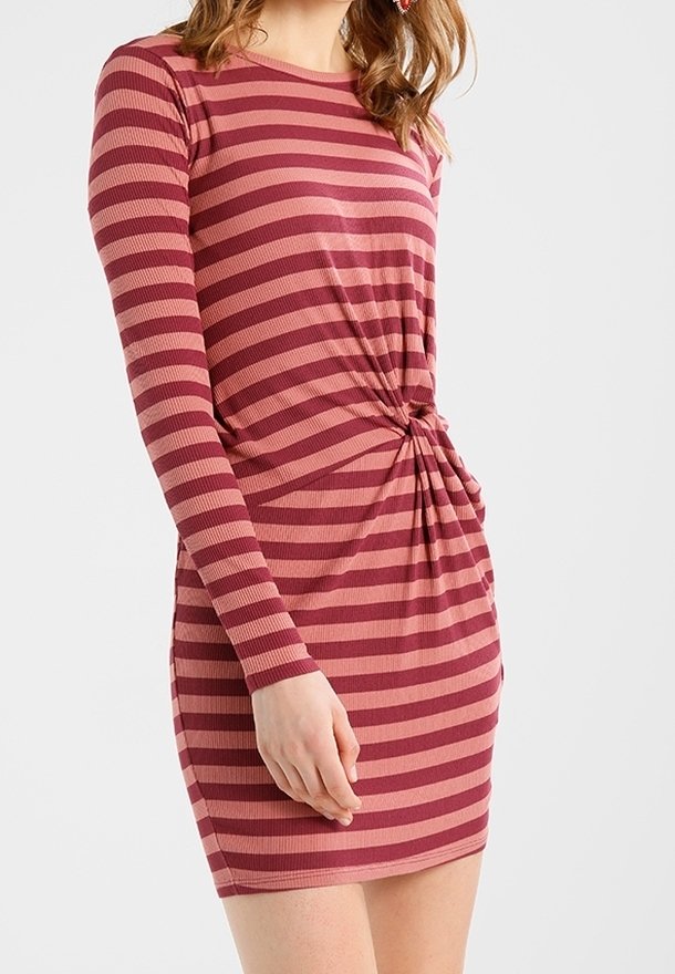 Femme portant une robe à manches longues à rayures horizontales roses et bordeaux avec un détail de nœud froncé à la taille.