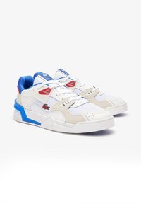 Zapatillas deportivas blancas que presentan una combinación de texturas suaves y de ante, acentos en azul y rojo, una suela gruesa y detalles perforados.