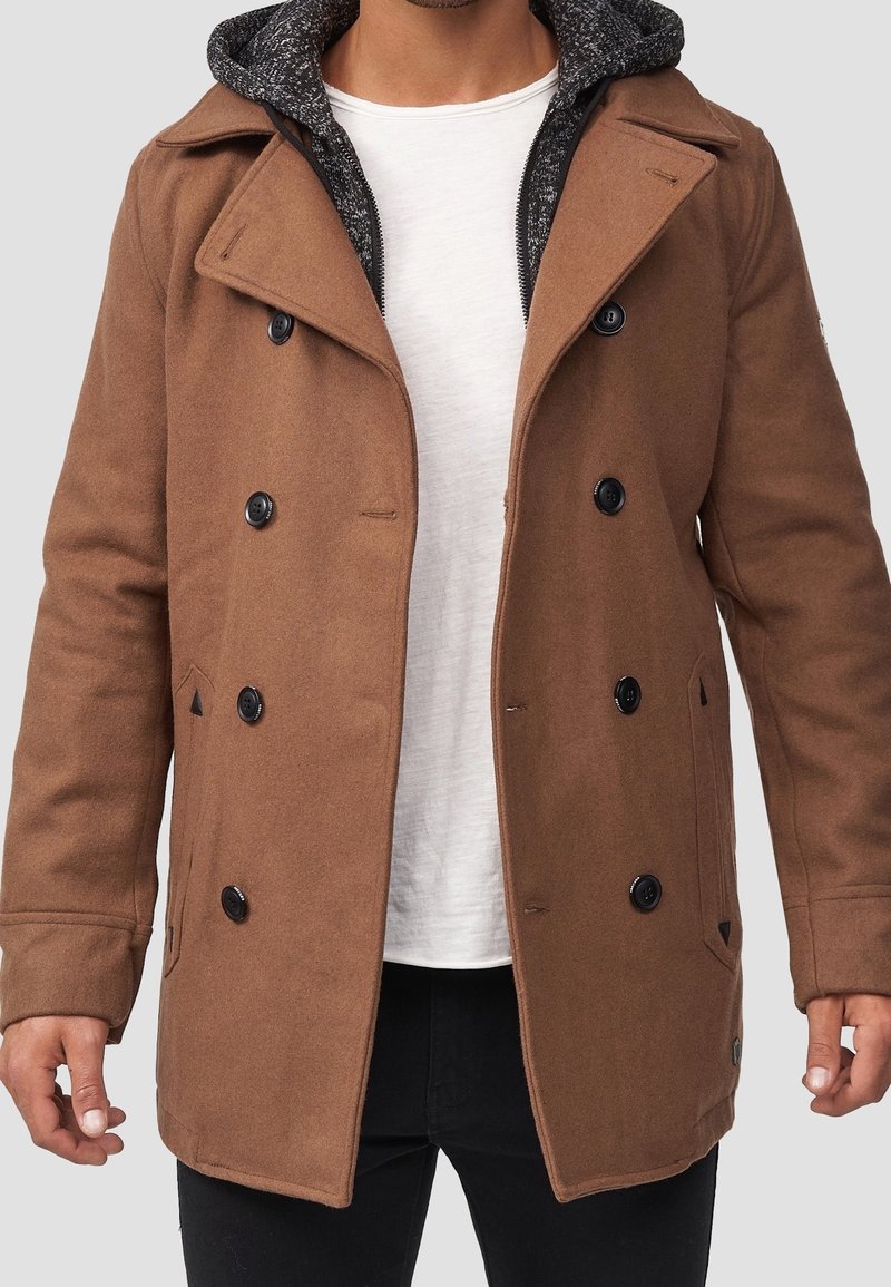 Brun peacoat lavet af uldblanding med dobbeltradet design, sorte knapper og grå hættefor. Lommeposer på siden.