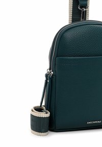 Donkergroene, getextureerde leren crossbodytas met dubbele ritsen, een voorvak en een brede stoffen band met beige randen en zilveren merkembleem.