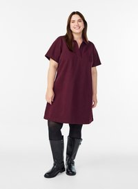 Robe bordeaux à manches courtes avec un col, dotée d'une coupe droite et de poches latérales. Assortie à des bottes noires jusqu'au genou.