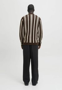 Braun- und cremefarben gestreifter Pullover mit vertikalen Streifen, gerippter Textur, Rundhalsausschnitt und schmalen Bündchen. Kombiniert mit weiten schwarzen Hosen.