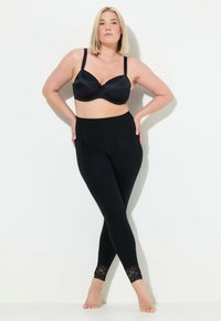 Zwarte leggings met kantdetails aan de mouwen, gecombineerd met een zwarte gewatteerde beha. Glad textuur, aansluitend design en elastische tailleband.