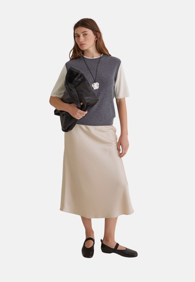 Top de manga corta en colores gris y crema, falda de satén beige, zapatos planos negros y un gran bolso negro con un acabado texturizado.