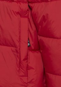 Rød boblejakke med quiltet design, med en sidelomme og en glatt, skinnende tekstur. Indre etikett synlig i lommen.