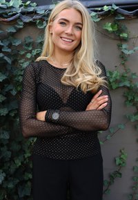 Čierny sieťovaný top so zlatými bodkami, dlhé rukávy, priliehavý strih. Kombinovaný s čiernymi nohavicami a hodinkami so strieborným ciferníkom a čiernym remienkom.