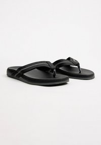 Chancletas negras con suela de goma plana, que presentan dos correas cruzadas y una planta texturizada. Las correas tienen detalles de costura en contraste.