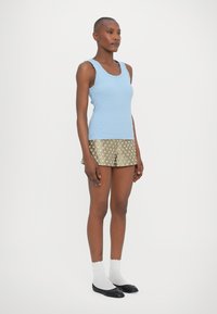 Svijetloplava rebrasta majica bez rukava s valovitim rubovima, u kombinaciji sa zlatnim šortsevima s cvjetnim uzorkom. Model nosi bijele čarape i crne balerinke.