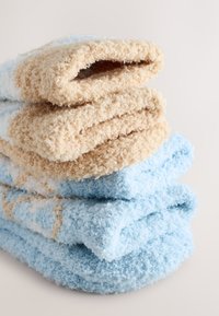 Soft, fluffy towels stacked, featuring sandy beige, light blue, and white colors with a textured surface. Each towel has a folded edge.