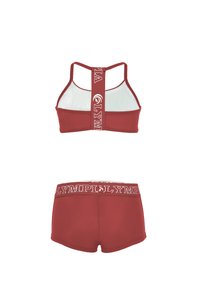 Sarkans sporta krūšturis ar baltu sietiņa aizmuguri un logo joslu, kopā ar saderīgiem augstām shorts ar baltu logo jostu.