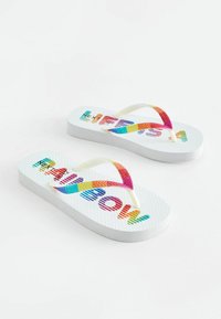 Des tongs blanches avec des semelles texturées, dotées de brides en caoutchouc multicolores et du texte "MEOW" en rayures multicolores sur la semelle.