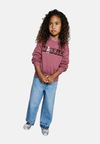Sweat-shirt rose avec le texte "Minnie" et un graphisme du personnage. Jeans bleu à large jambe. L'enfant porte des ballerines argentées et a les cheveux bouclés.