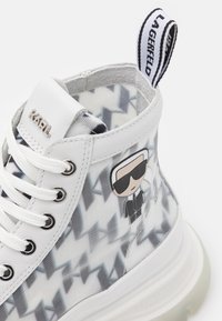Sneaker alte con una tomaia in pelle bianca e pannelli trasparenti che presentano un motivo geometrico grigio. Include un charm decorativo.