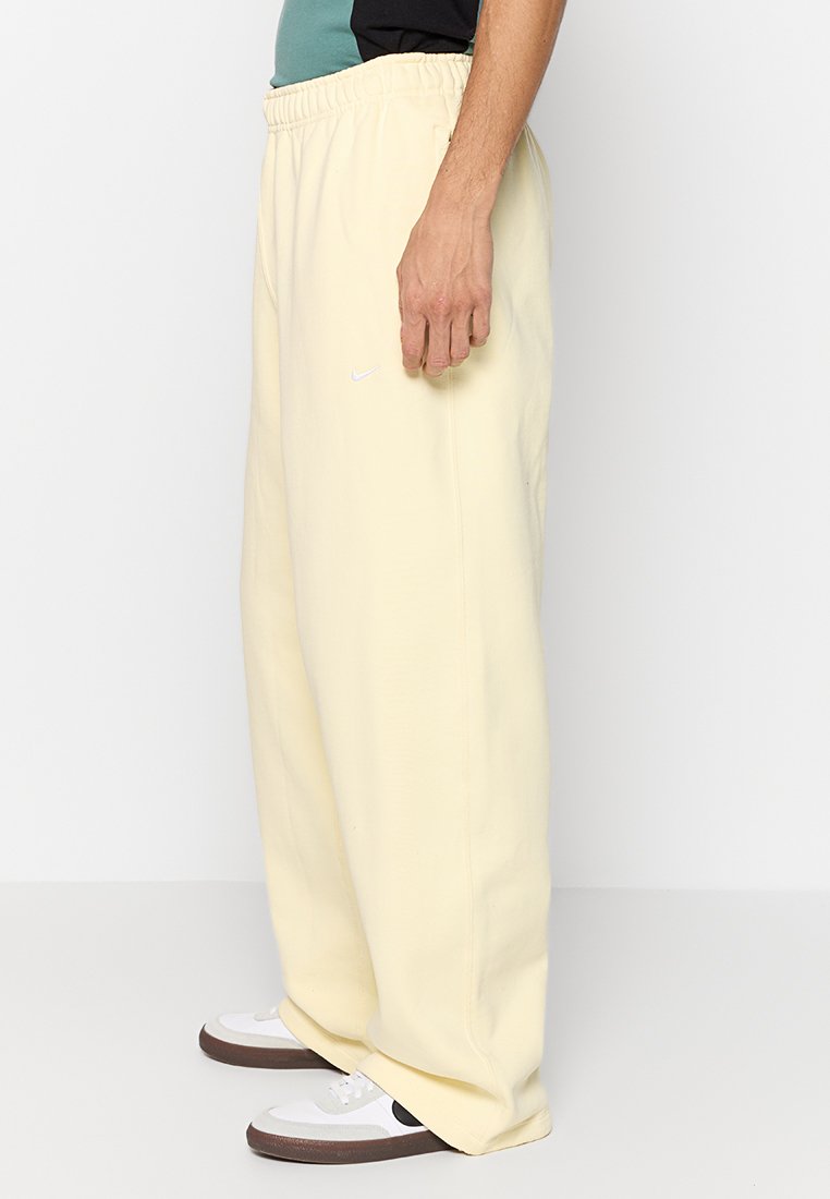 Pantalones de chándal amarillos con un corte relajado, cinturilla elástica y logo de Nike blanco en el costado. Combinados con zapatillas blancas que presentan acentos oscuros.