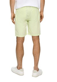 Lichtgroene short met een gladde textuur, knie-lengte, met achterzakken, gedragen met witte sneakers. Eenvoudig ontwerp, minimalistische stijl.