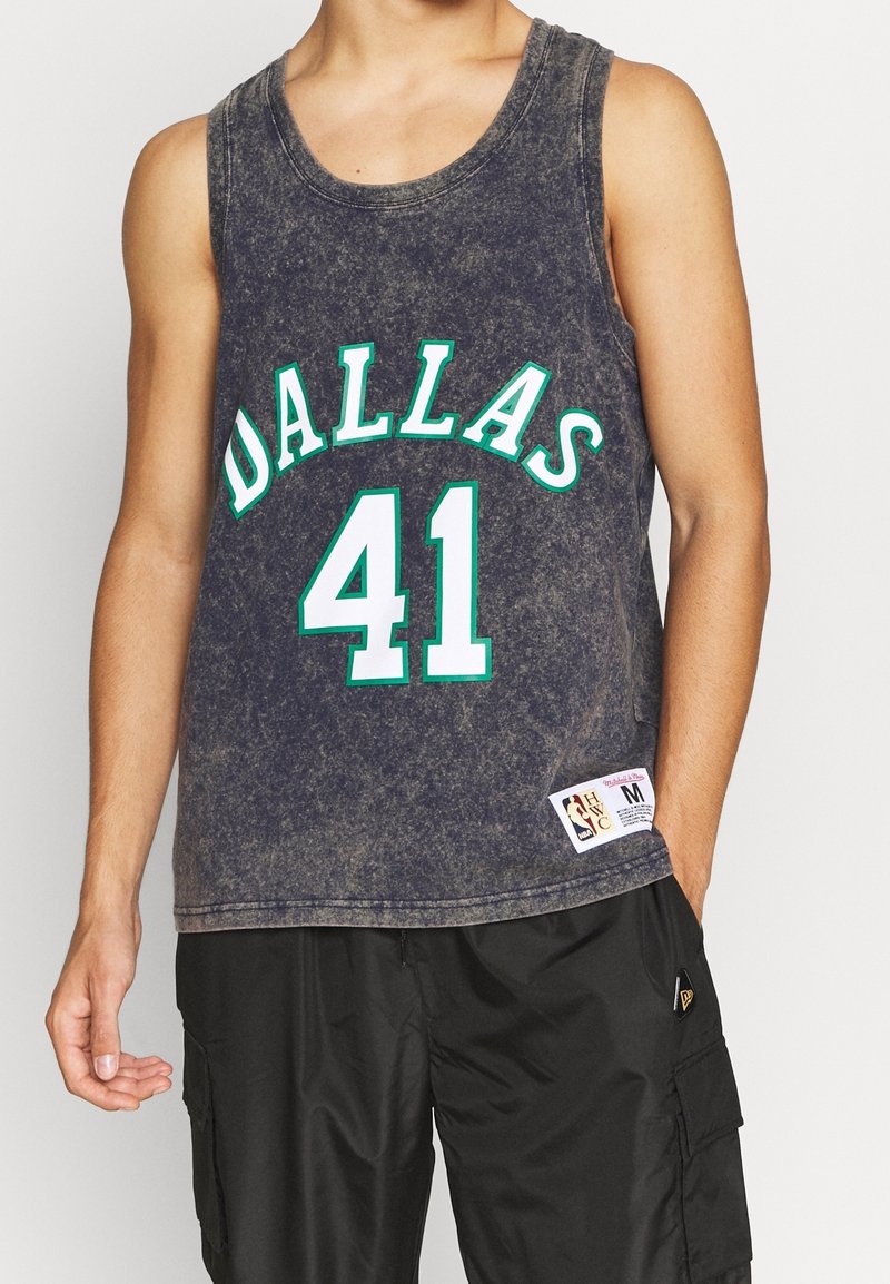 Maillot de basket sans manches noir délavé de Dallas avec le numéro 41 porté par une personne portant un short cargo noir, main détendue le long du corps.