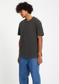 Donkergrijze katoenen t-shirt met korte mouwen, ronde hals en een klein embleem op de borst, gecombineerd met losse blauwe spijkerbroek.