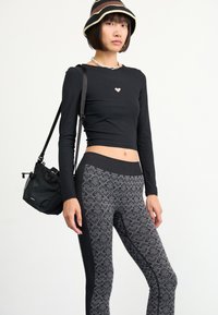 Top corto de manga larga de canalé negro con logo de corazón, combinado con leggings grises de patrón que tienen paneles laterales negros. Se incluye un pequeño bolso negro.