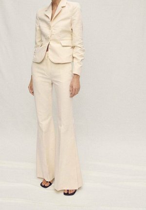 Person wearing a cream tailored blazer and matching flared trousers, paired with black square-toe heeled sandals.
