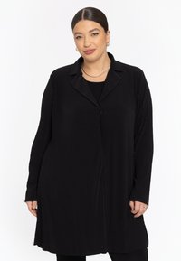 Schwarze Longline-Hemdjacke mit Reverskragen, strukturiertem vertikalem Rippenmuster und Knopfverschluss. Lange Ärmel mit lockerer Passform.
