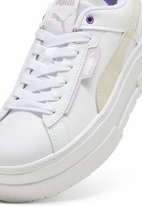 Sneaker bianchi in pelle con accenti viola, dotate di un dettaglio in suede beige texture, lacci bianchi e una suola in gomma spessa. Marchio PUMA visibile.