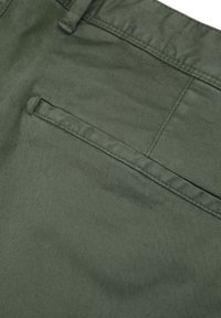 Olivgrüner Stoff mit glatter Textur. Verfügt über eine einzelne Gesäßtasche mit sorgfältig gesteppten Kanten. Minimalistisches Design mit subtilen Details.