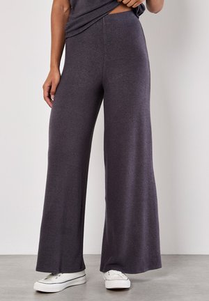Lässig geschnittene, weit geschnittene Hose aus dunkelgrauem Stoff mit weicher Textur, mit hohem Bund und kombiniert mit weißen Sneakers.