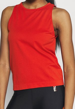 Kvinde iført ærmeløs rød sportstop og sorte leggings med logo på taljebåndet, vist fra skuldre til hofter.
