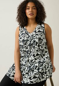 Blommig ärmlös topp i svart och vitt med V-hals, som har ett texturerat tyg och ett mönster av blad över hela plagget.