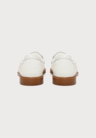 Paire de chaussures habillées en cuir blanc avec talons empilés marron vues de dos sur un fond clair uni.