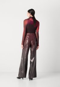 Doorzichtige lange mouwtop die overgaat van donkerrood naar zwart, gecombineerd met hooggetailleerde, wijde burgundy leren broek met een gladde textuur.