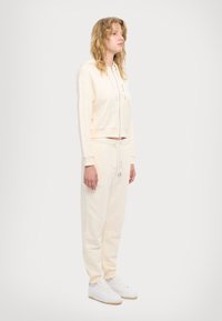 Krémová skrátená mikina s predným zipsom, spojená s ladnými teplákmi. Biele tenisky dotvárajú outfit. Mäkká tkanina a uvoľnený strih.