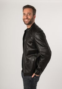 Giacca in pelle nera con chiusura a zip e tasche laterali. Tessuto liscio, design aderente e cuciture sulle spalle visibili.