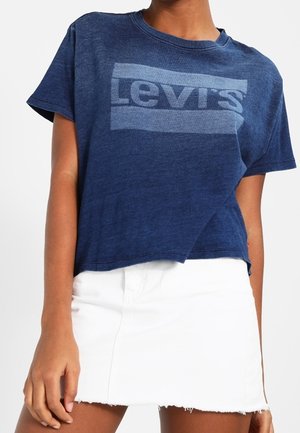 Person iført en blå Levi's cropped t-shirt og en hvid denimnederdel med rå kant.