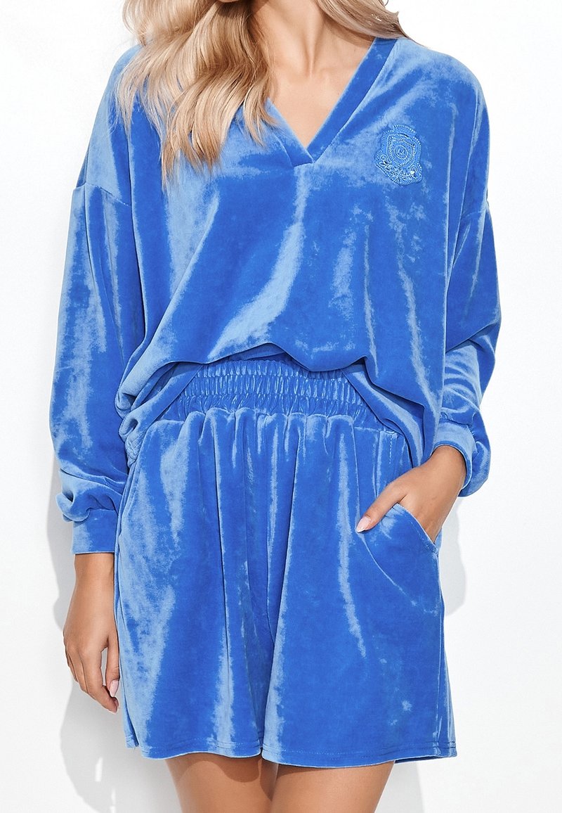 Femme portant un haut ample en velours bleu à manches longues avec col en V et un short assorti à taille élastique avec poches latérales.
