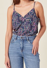 Navy blue camisole with a paisley pattern in pink and green, featuring thin shoulder straps. Paired with high-waisted light blue jeans.