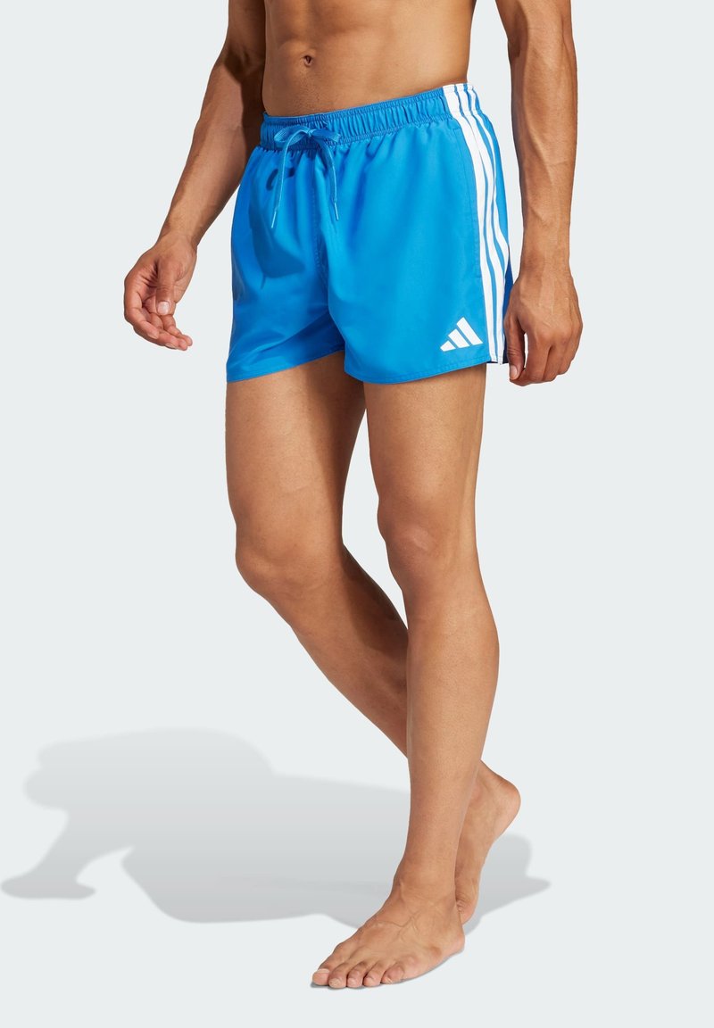 Bañador azul hecho de material ligero con cintura ajustable, que presenta tres rayas blancas a lo largo del lado y un logo de Adidas.