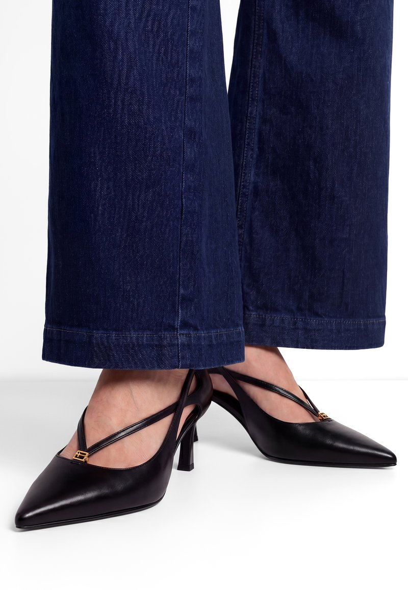 Μαύρες δερμάτινες γόβες Slingback με μυτερή μύτη, λεπτές λουράκια και χρυσή λεπτομέρεια, συνδυασμένες με σκούρο μπλε τζιν παντελόνια με ευρύ μπατζάκι.