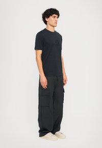 T-shirt preta de mangas curtas com um logo discreto, combinada com calças cargo pretas de corte largo e muitos bolsos, usadas com ténis brancos.