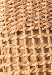 Naturalny pleciony koszyk w jasnym beżowym kolorze z przeplatanymi włóknami, prezentujący teksturowaną powierzchnię i wzór w kratkę.