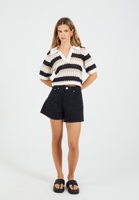 Sweter na druty w czarno-kremowe paski, z krótkimi rękawami i dekoltem w serek; połączony z czarnymi szortami o wysokim stanie i masywnymi czarnymi sandałami.