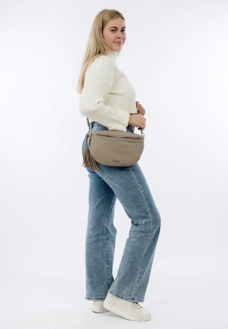Beige Leder Umhängetasche mit Fransen, silbernem Reißverschluss und verstellbarem Gurt. Getragen mit hellblauen Schlagjeans und weißen Sneakers.