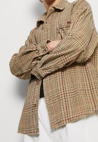 Tan geruite shirt met een knoopsluiting, voorzien van lange mouwen, een relaxte pasvorm en een subtiele rode accent logo op de borst.