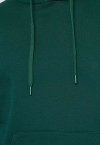 Haut à capuche vert en tissu doux, avec des cordons de serrage, une poche avant et une finition texturée.