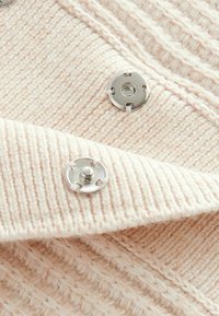 Tissu tricoté rose clair avec des côtes horizontales et verticales. Boutons-pression métalliques à l'avant, présentant une surface lisse et des fils apparents.