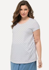 Top blanco de manga corta con lunas azules, escote redondo y fruncido en los laterales, combinado con pantalones azules. Tejido de algodón suave.