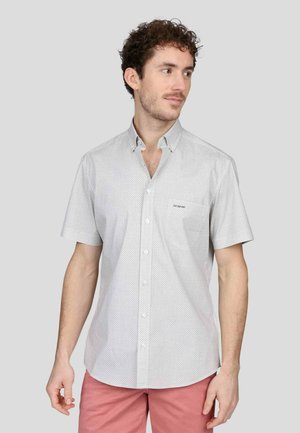 Chemise à manches courtes, blanche, avec un petit motif à pois, comportant un col et une poche poitrine. Texture de tissu lisse.