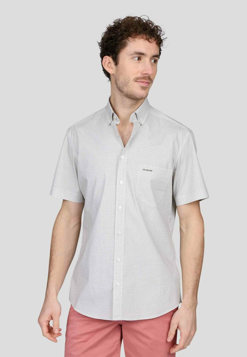 Chemise à manches courtes, blanche, avec un petit motif à pois, comportant un col et une poche poitrine. Texture de tissu lisse.